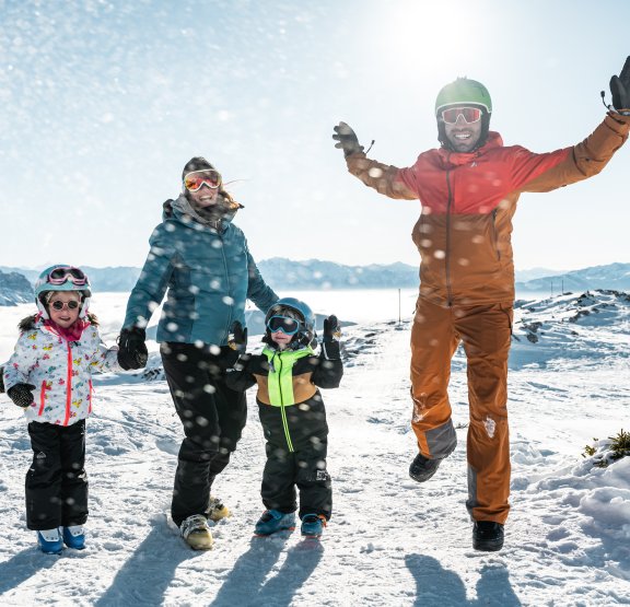 Famille avec jeunes enfants sautant devant un paysage enneigé