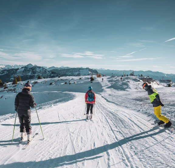 Groupe de jeunes skieurs et snowboarder qui skient avec un ciel bleu en fond